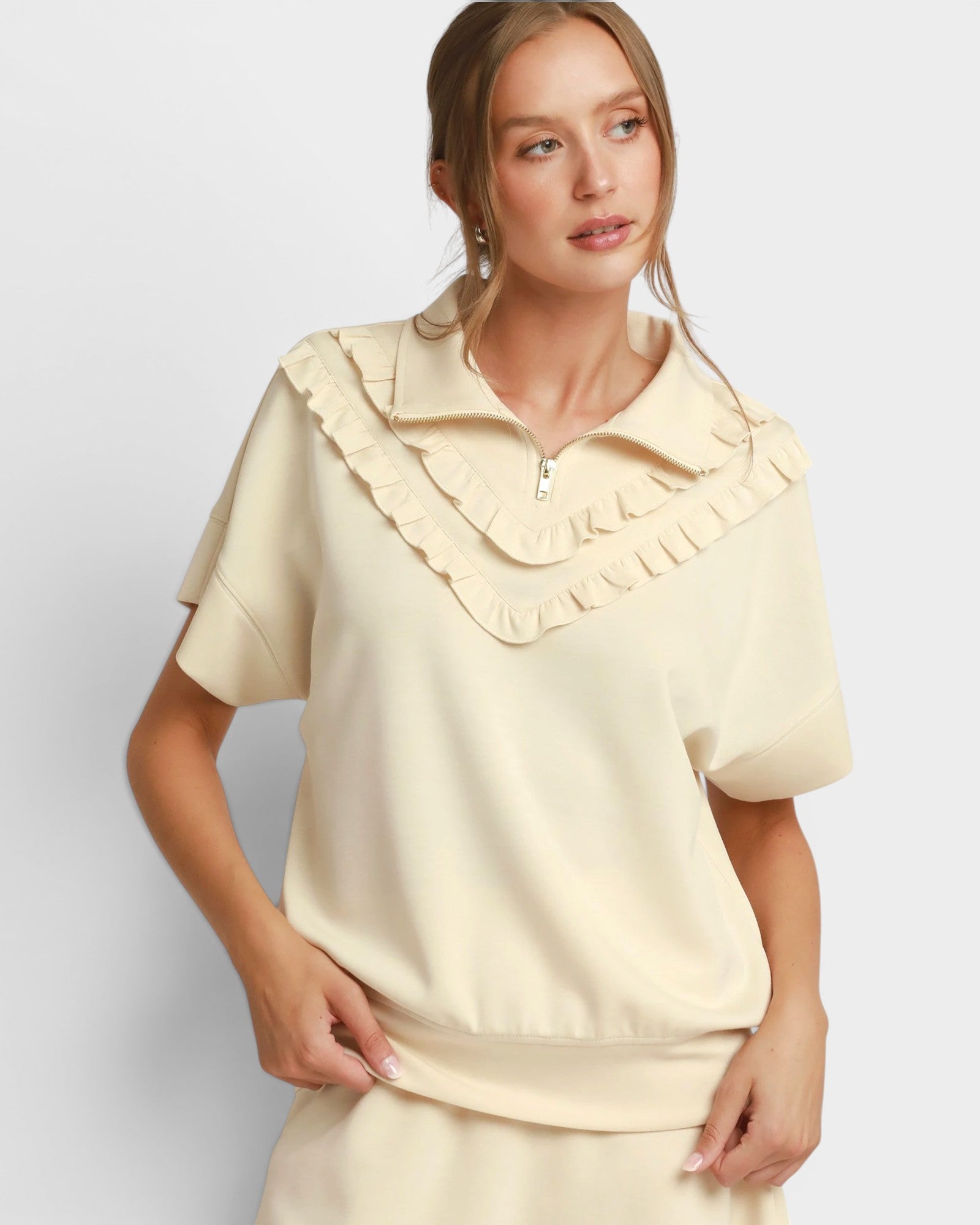 Woman wearing a beige blouse with ruffled collar on a light gray background