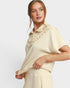 Woman wearing a beige outfit with ruffled details on a plain background