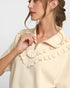 Woman wearing a beige blouse with ruffled collar against a light background