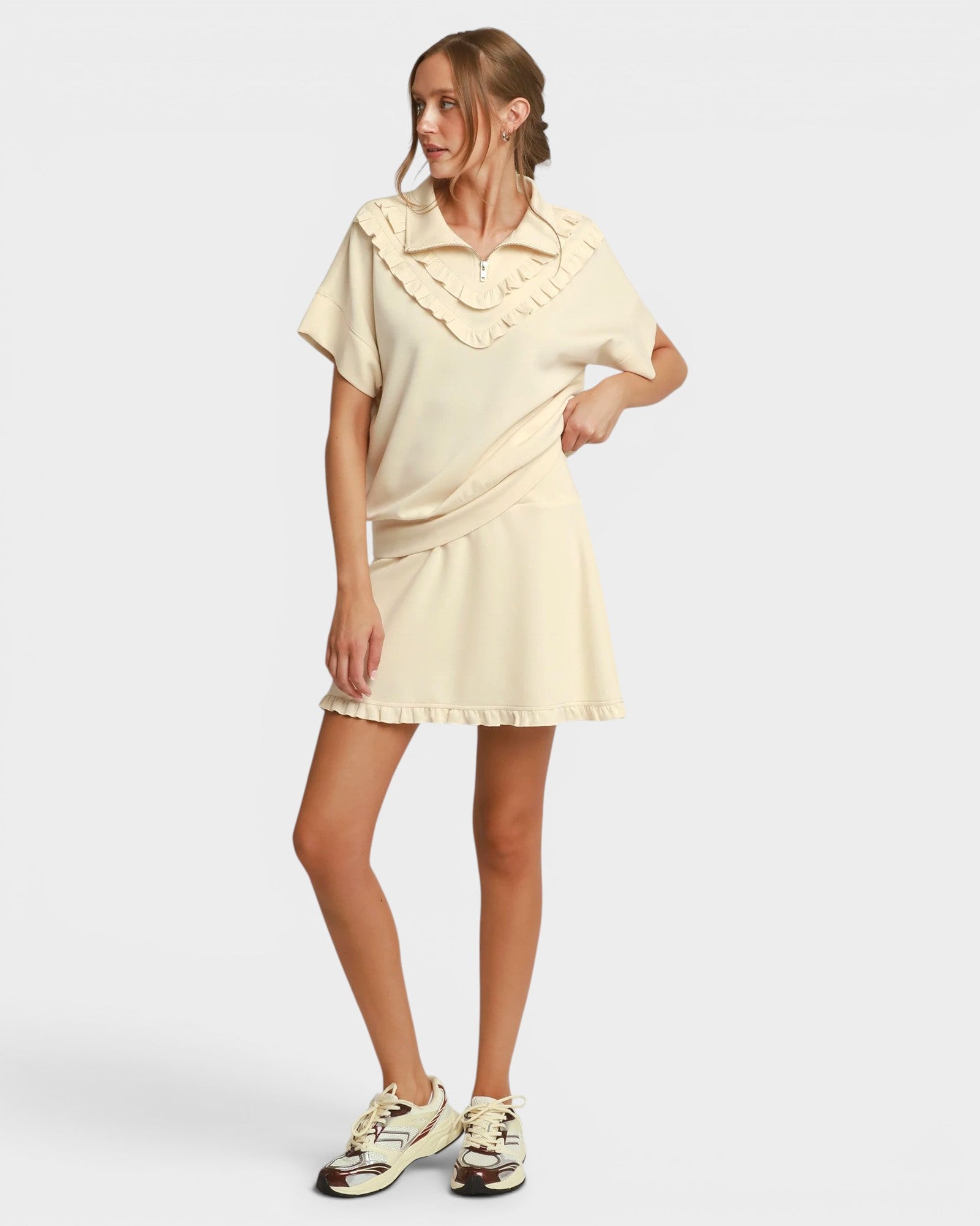 Woman wearing a light-colored dress with ruffled details on a plain background