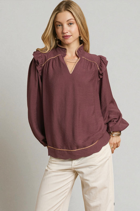 Woman wearing a burgundy blouse with ruffled sleeves on a plain background