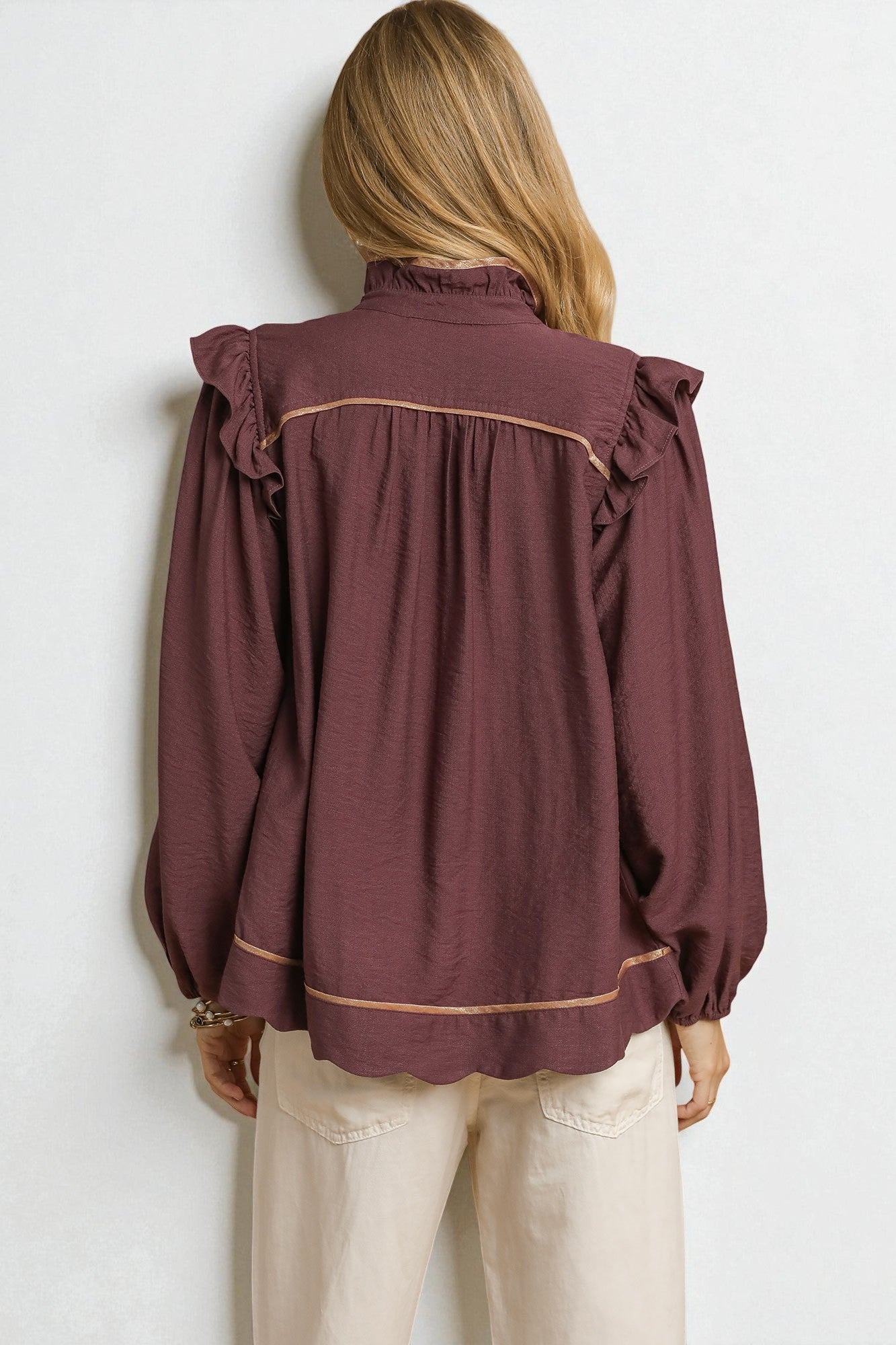 Person wearing a burgundy blouse with ruffled shoulders against a white background