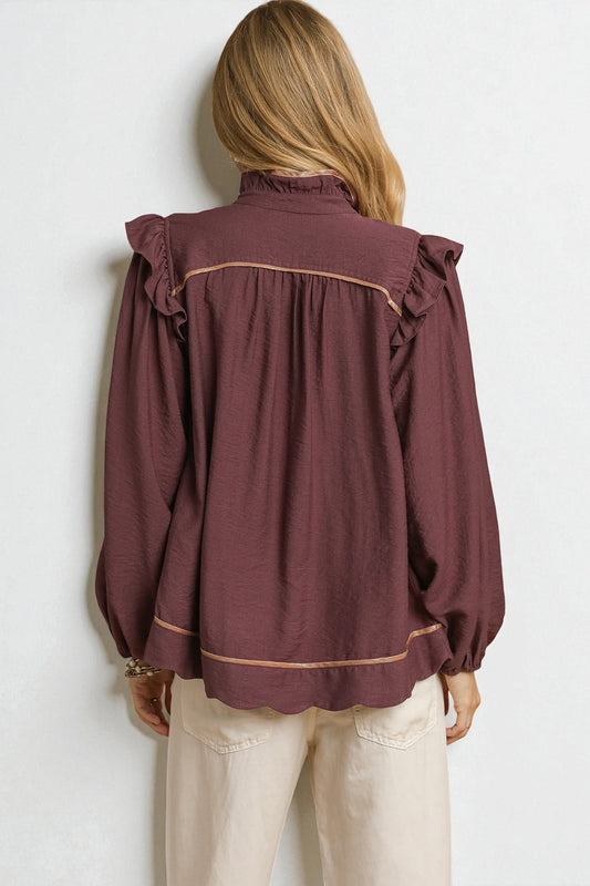 Person wearing a burgundy blouse with ruffled shoulders against a white background