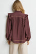 Person wearing a burgundy blouse with ruffled shoulders against a white background