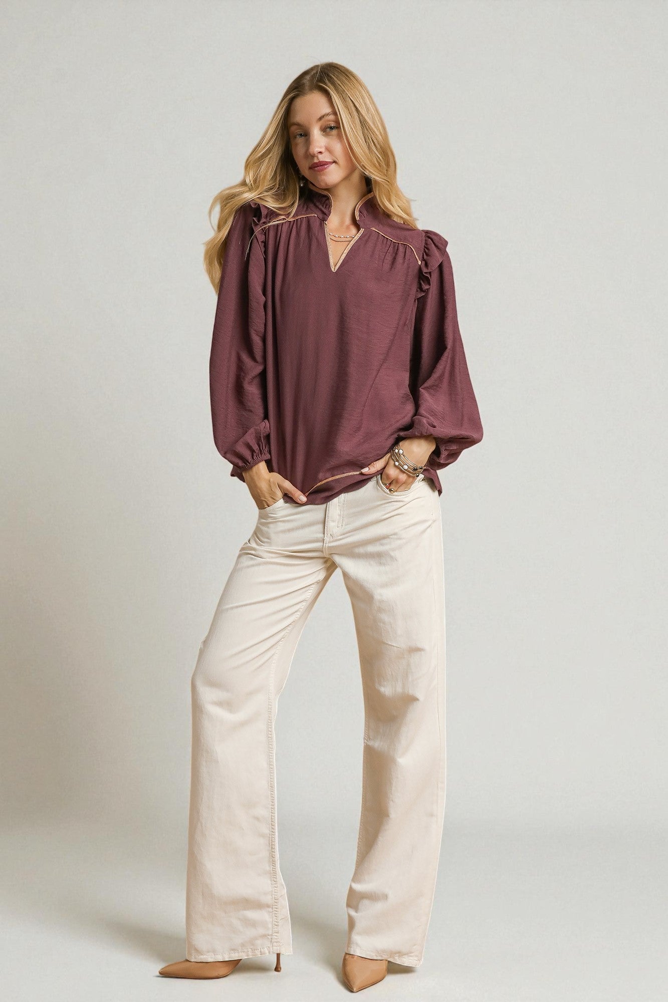 Woman wearing a burgundy blouse and beige pants against a plain background