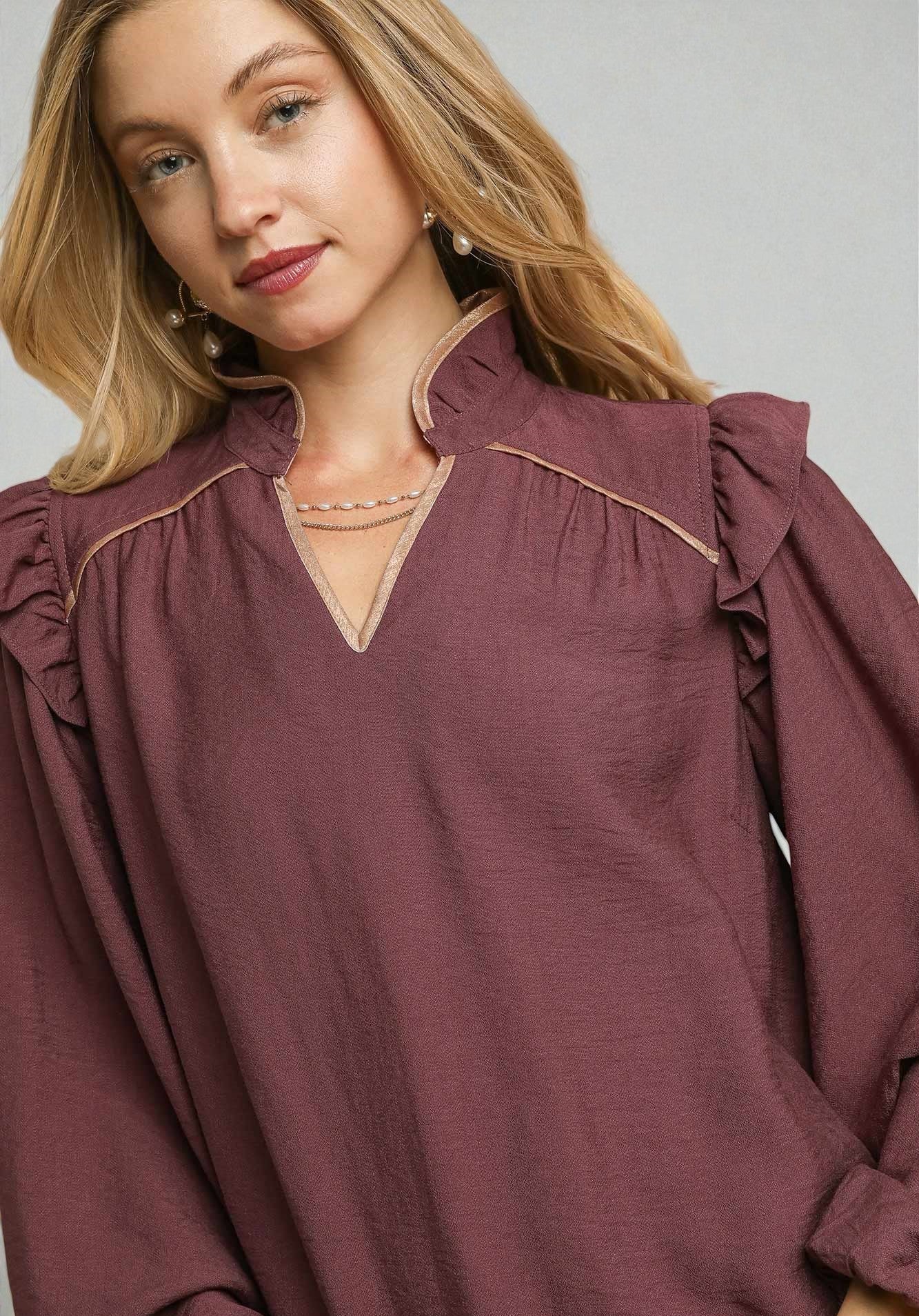 Woman wearing a burgundy blouse with ruffled shoulders on a gray background