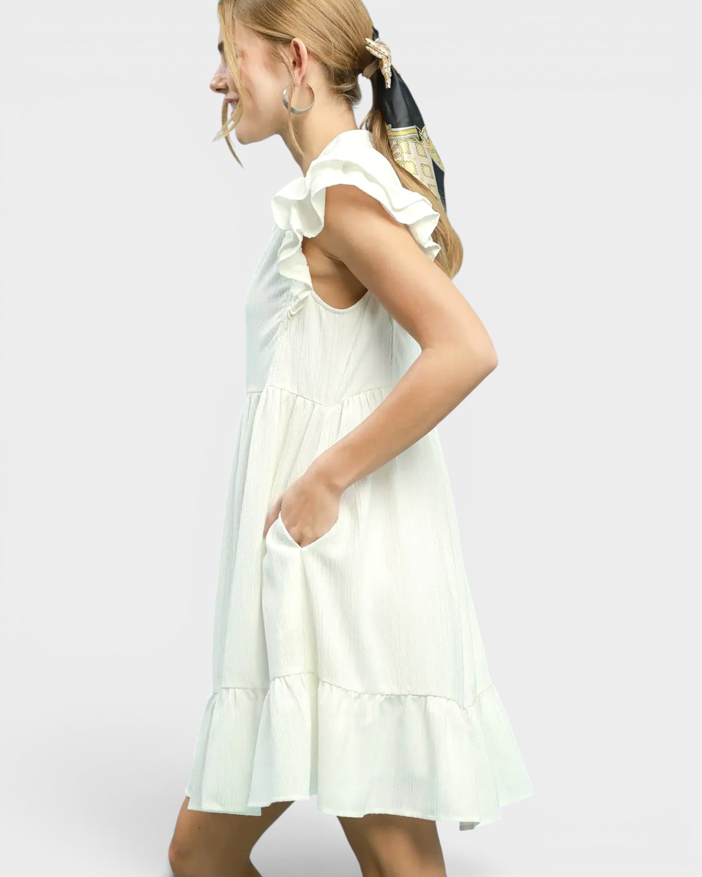 Woman wearing a white dress with ruffled sleeves on a plain background