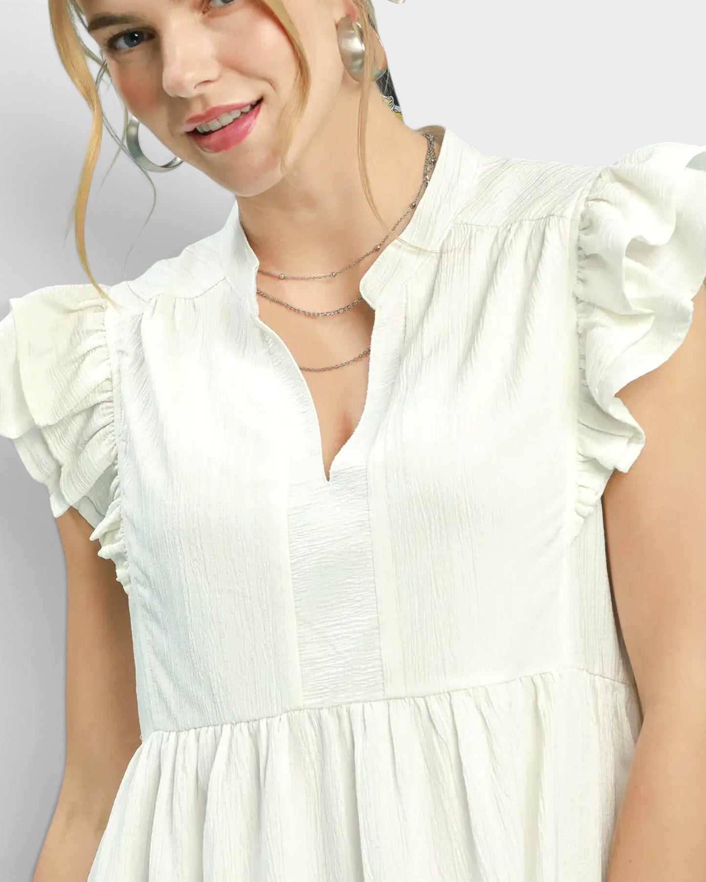 Woman wearing a white dress with ruffled sleeves on a light gray background