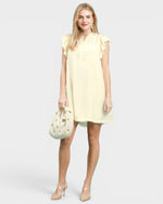 Woman wearing a light yellow dress holding a matching handbag on a white background