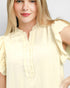 Woman wearing a light yellow blouse with ruffled sleeves on a plain background