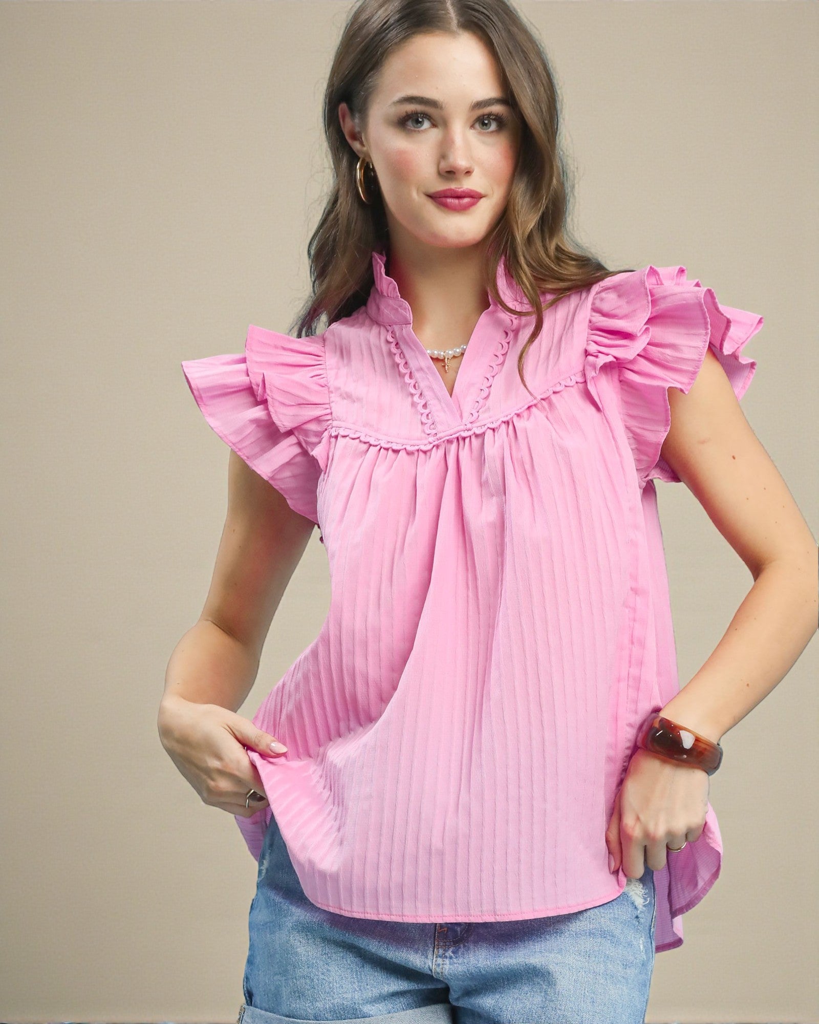 Woman wearing a pink blouse with ruffled sleeves against a beige background
