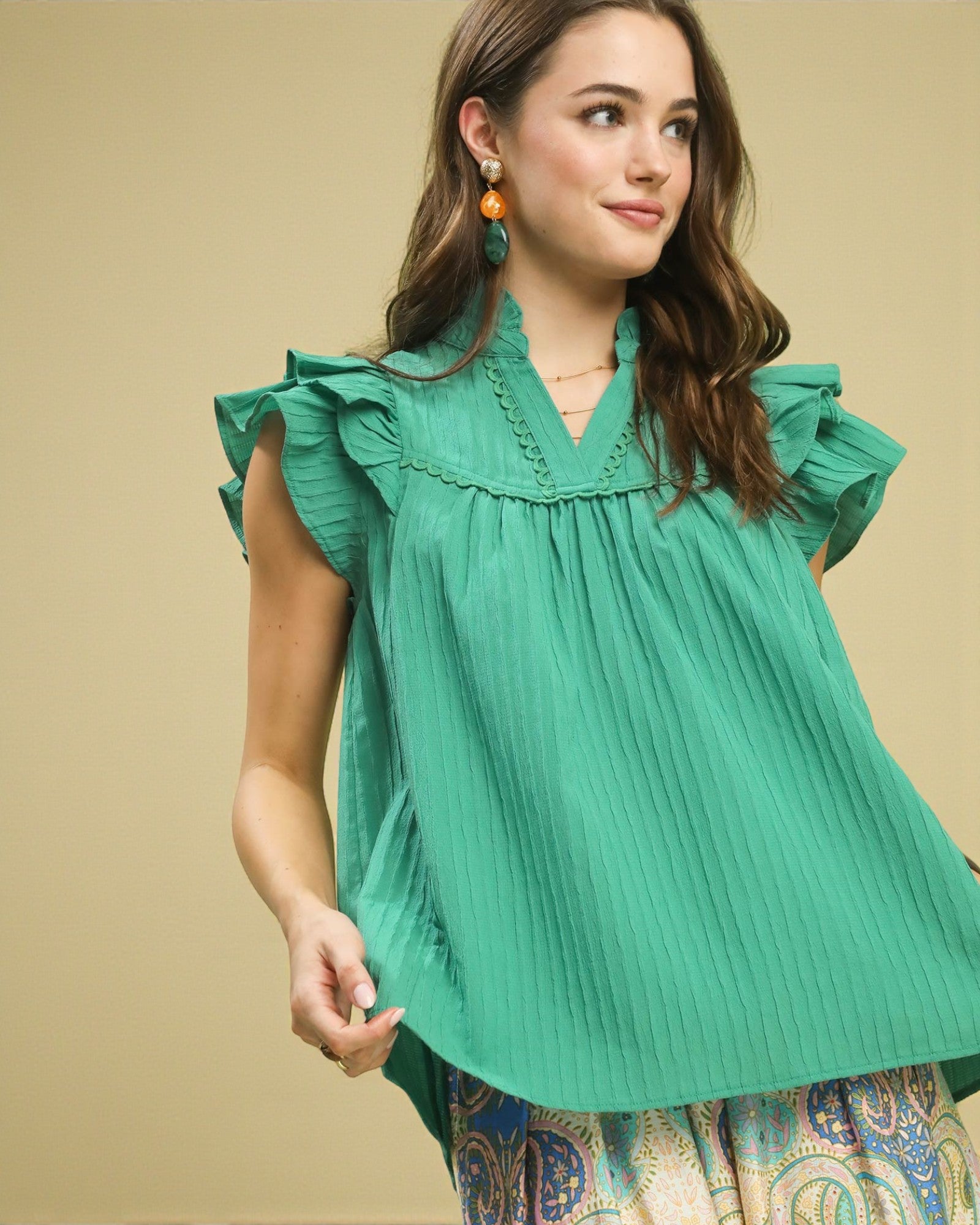 Woman wearing a green blouse with ruffled sleeves against a beige background