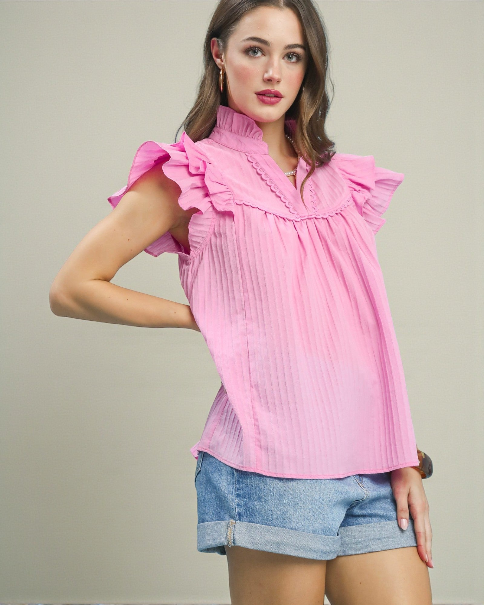 Woman wearing a pink blouse with ruffled sleeves and denim shorts on a neutral background