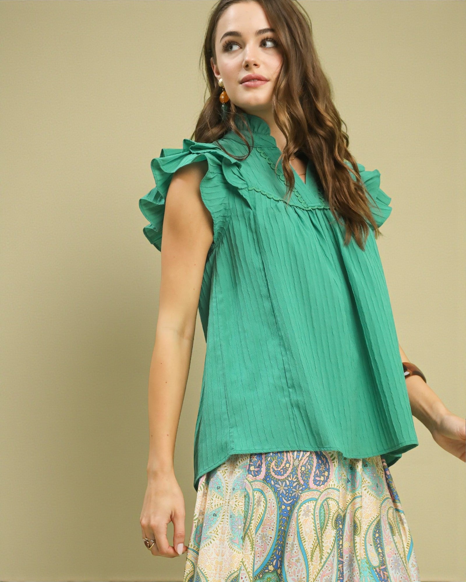 Woman wearing a green top with ruffled sleeves against a beige background