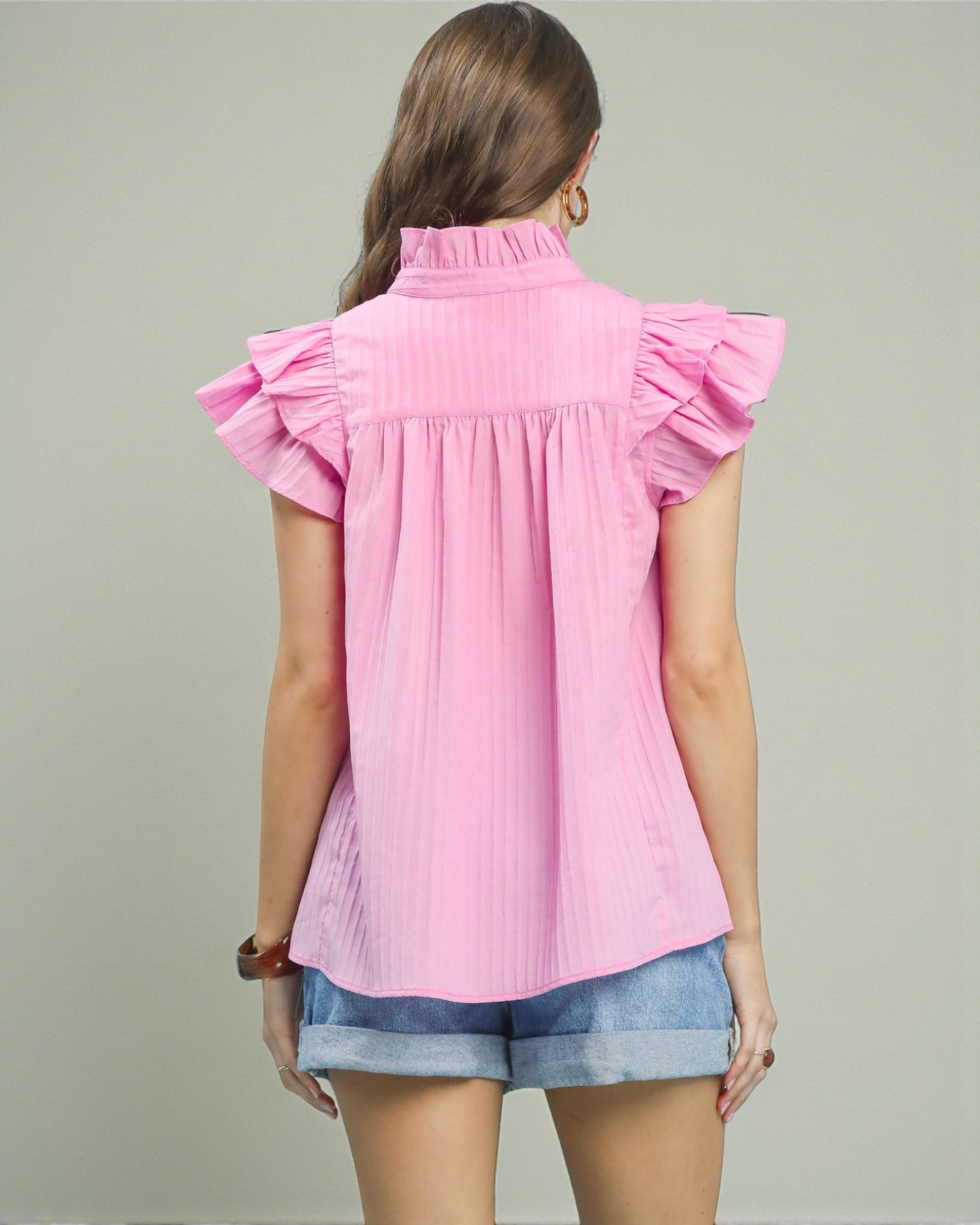 Woman wearing a pink blouse with ruffled sleeves on a plain background