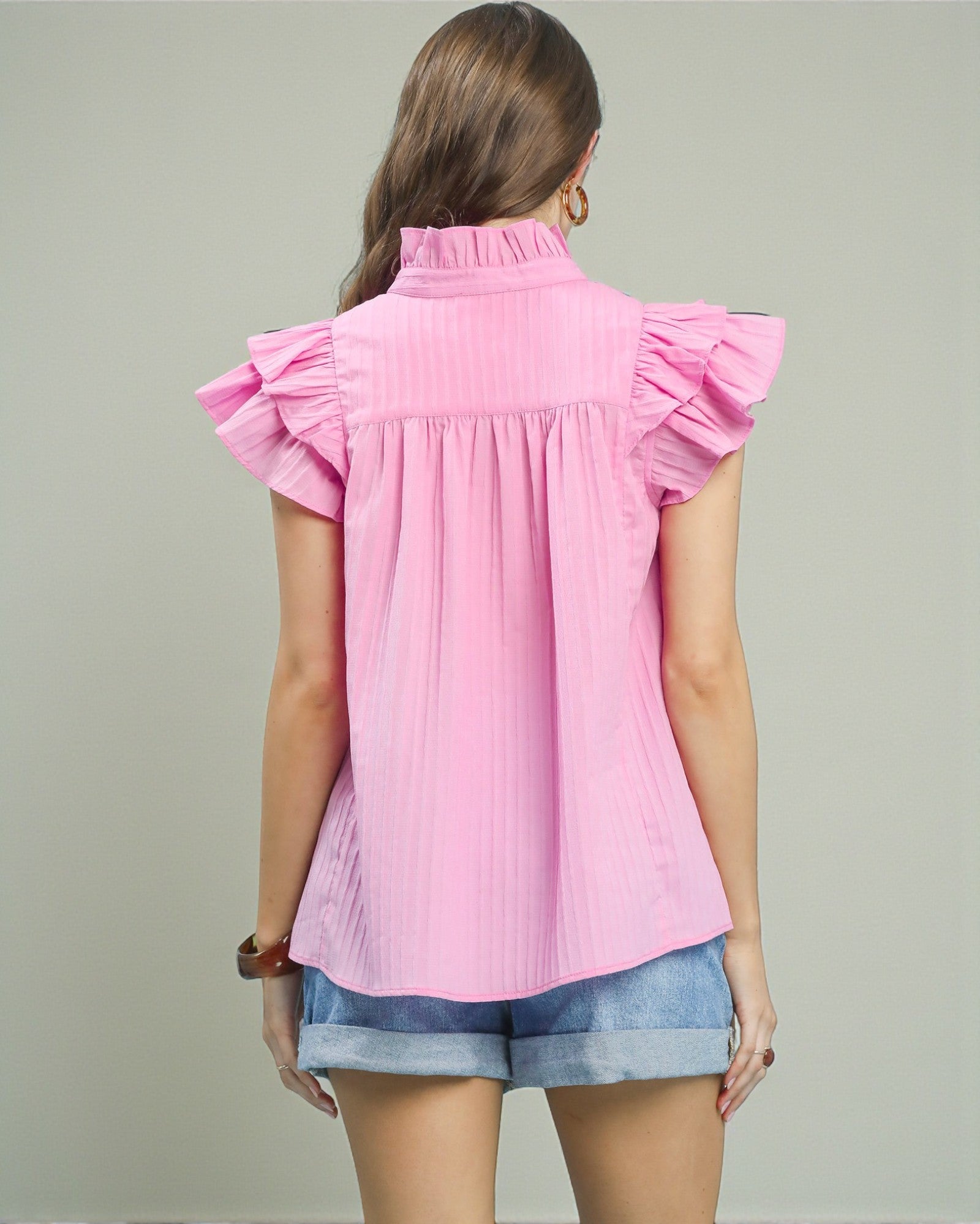 Woman wearing a pink blouse with ruffled sleeves on a plain background