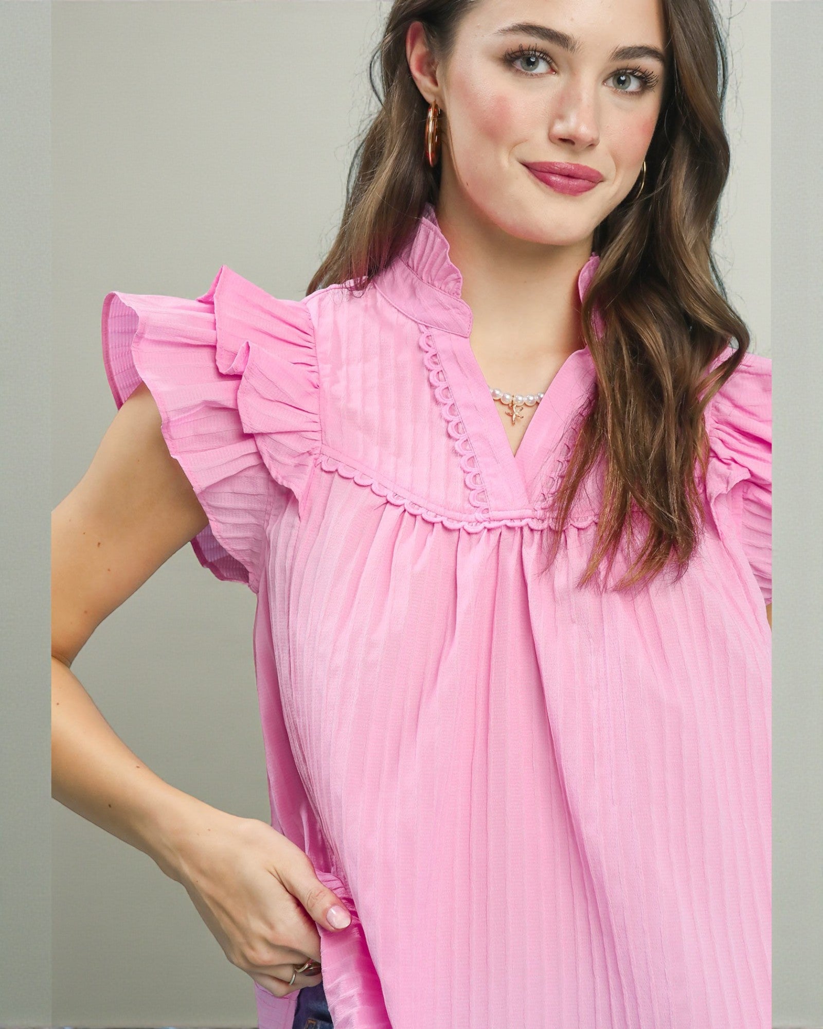 Woman wearing a pink dress with ruffled sleeves against a neutral background