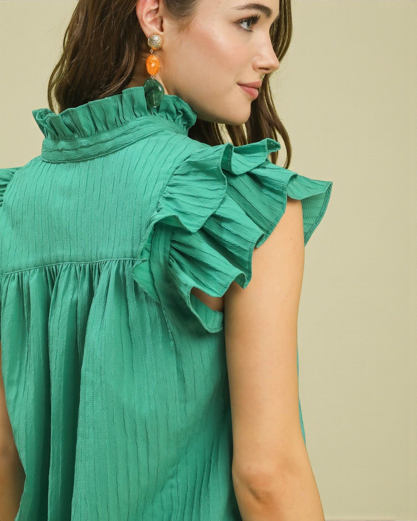Woman wearing a green blouse with ruffled sleeves on a beige background