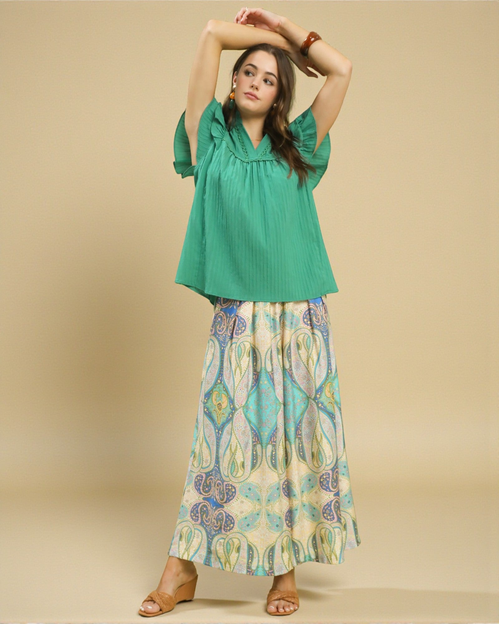 Woman wearing a green top and patterned skirt on a beige background