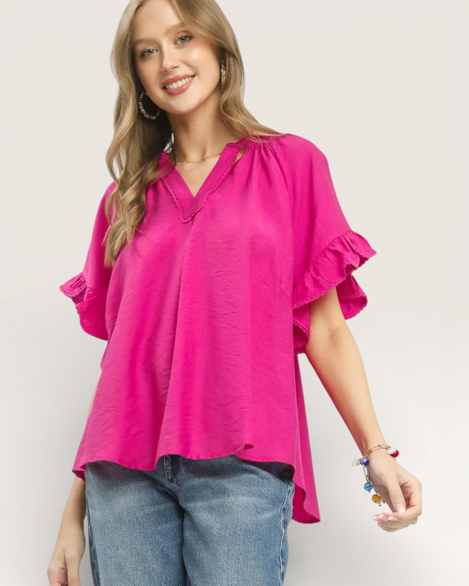 Woman wearing a bright pink blouse with ruffled sleeves on a plain background