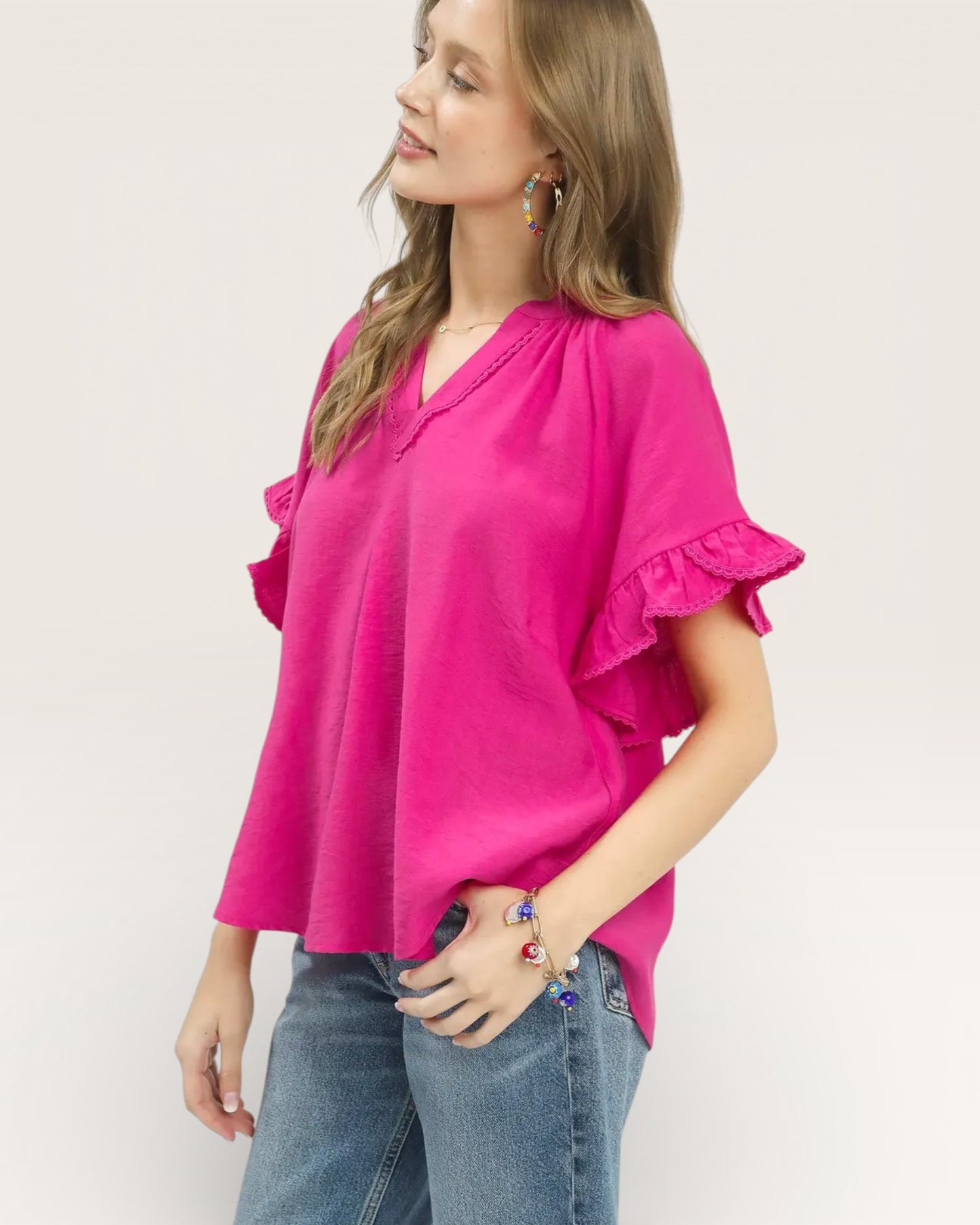 Woman wearing a bright pink blouse with ruffled sleeves on a plain background