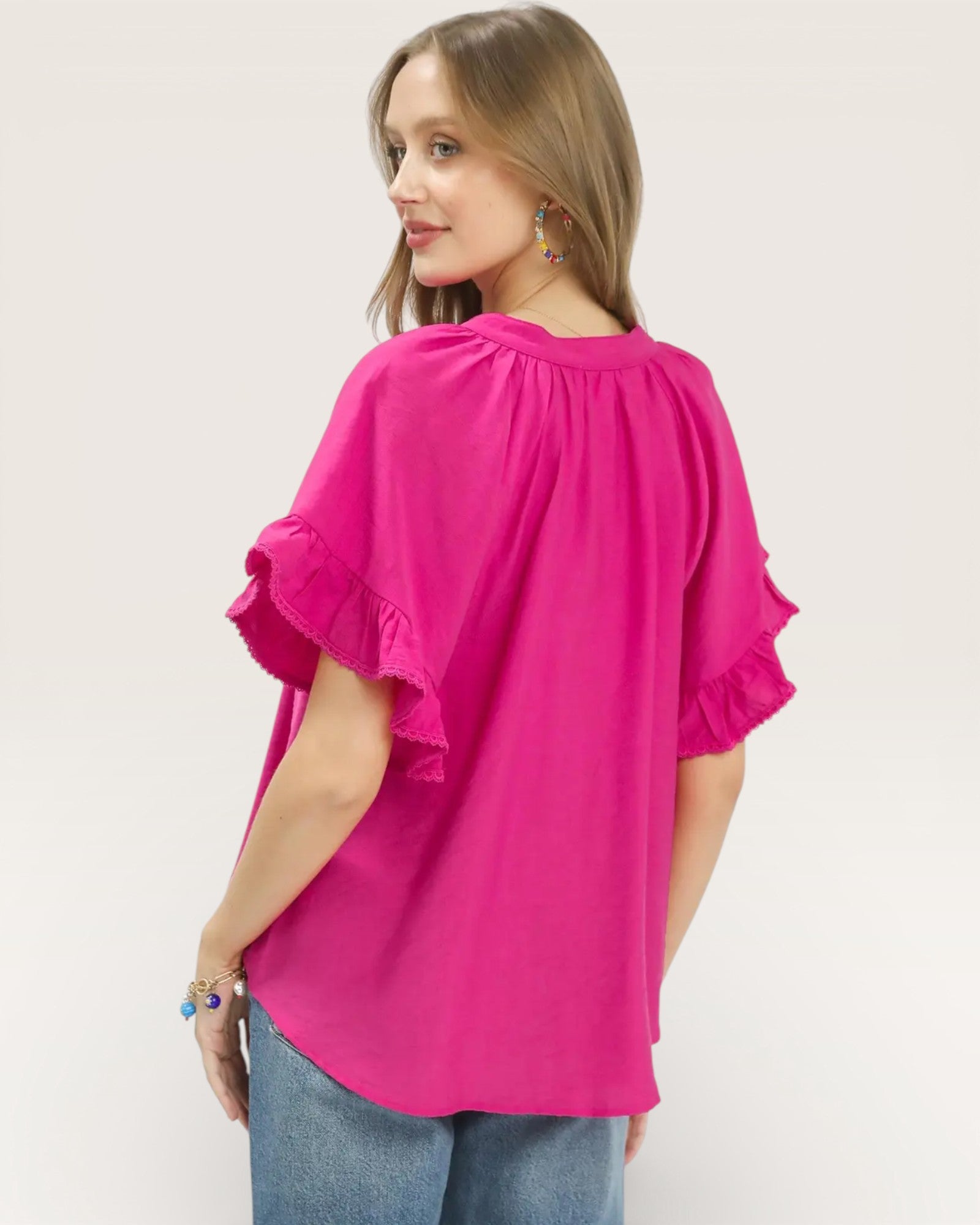 Woman wearing a bright pink blouse with ruffled sleeves on a white background