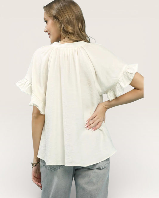 Woman wearing a white blouse with ruffled sleeves on a plain background