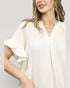 Woman wearing a white blouse with ruffled sleeves on a plain background