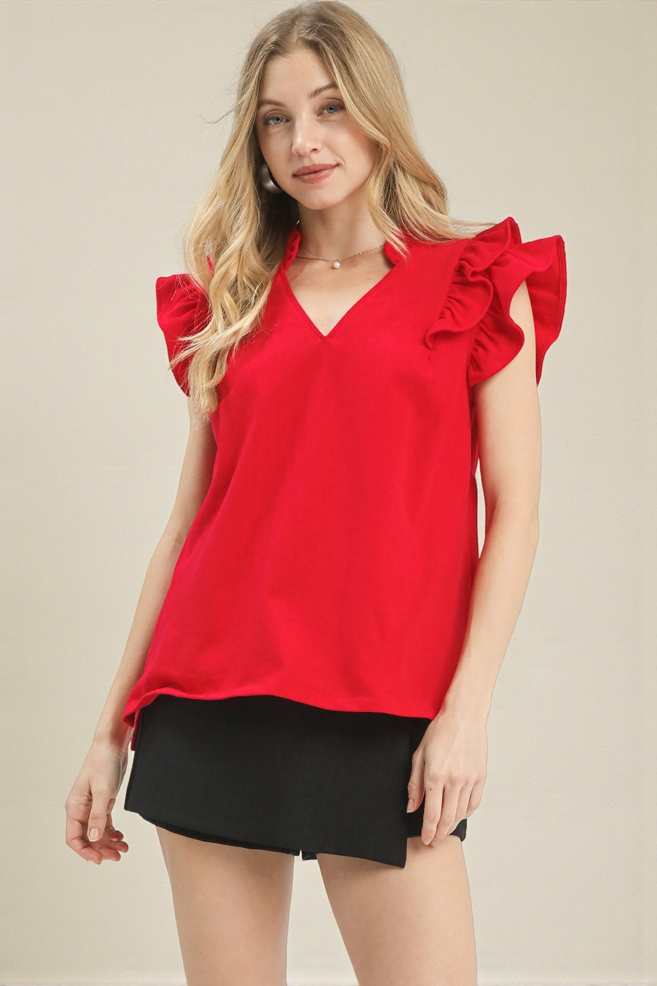 Woman wearing a red blouse with ruffled sleeves on a beige background