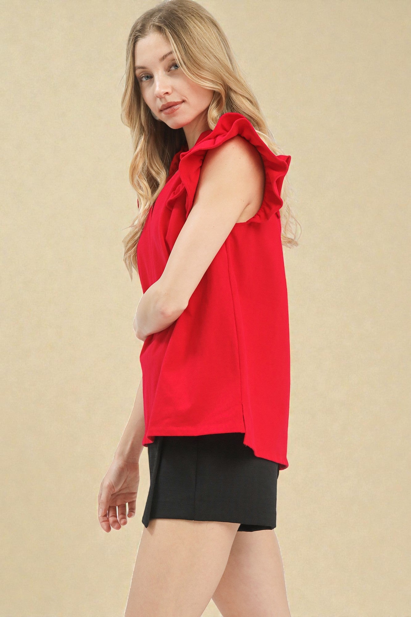 Woman wearing a red sleeveless top with ruffled shoulders against a beige background