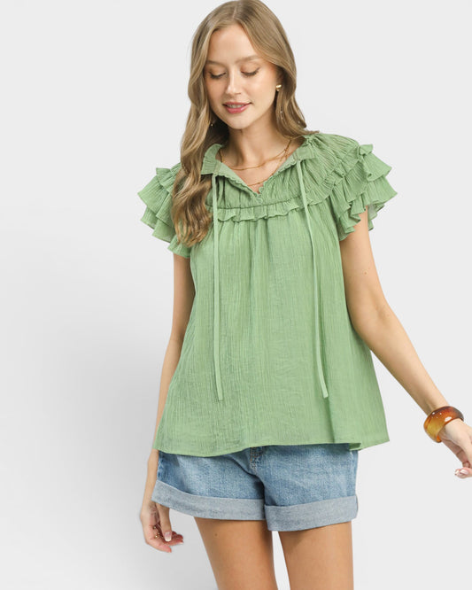 Woman wearing a green blouse with ruffled sleeves and denim shorts on a white background