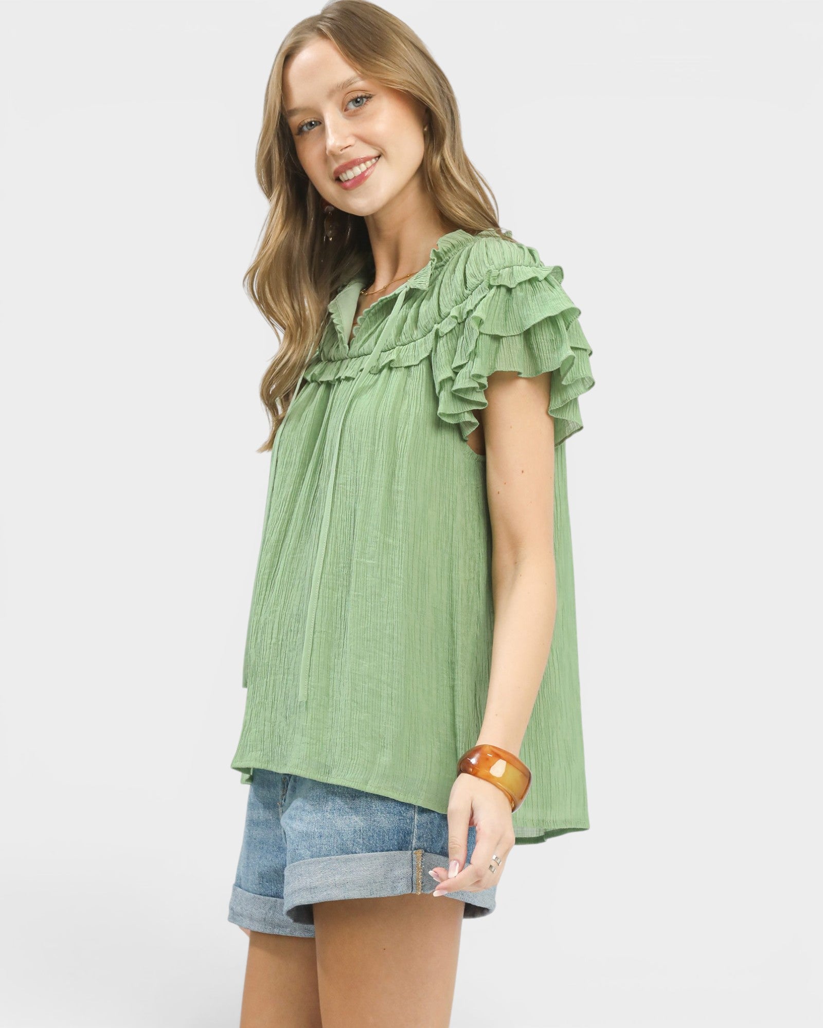 Woman wearing a green ruffled blouse and denim shorts on a white background