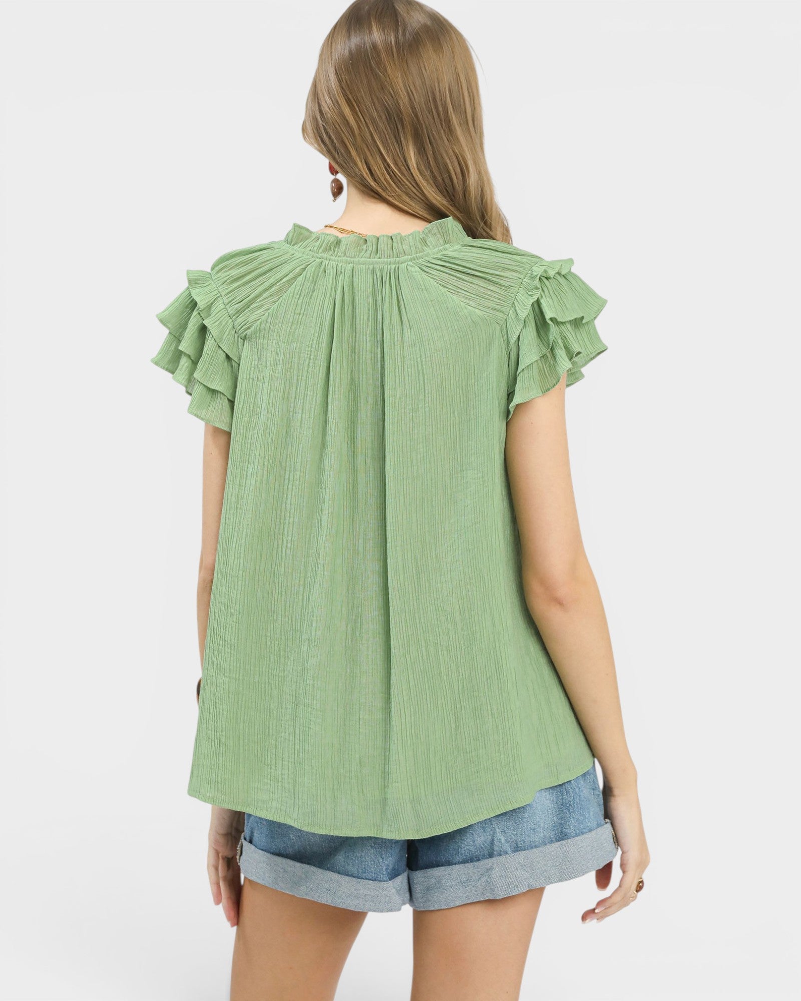 Woman wearing a green blouse with ruffled sleeves on a white background