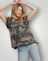 Woman wearing a black floral patterned top and light blue jeans against a plain background