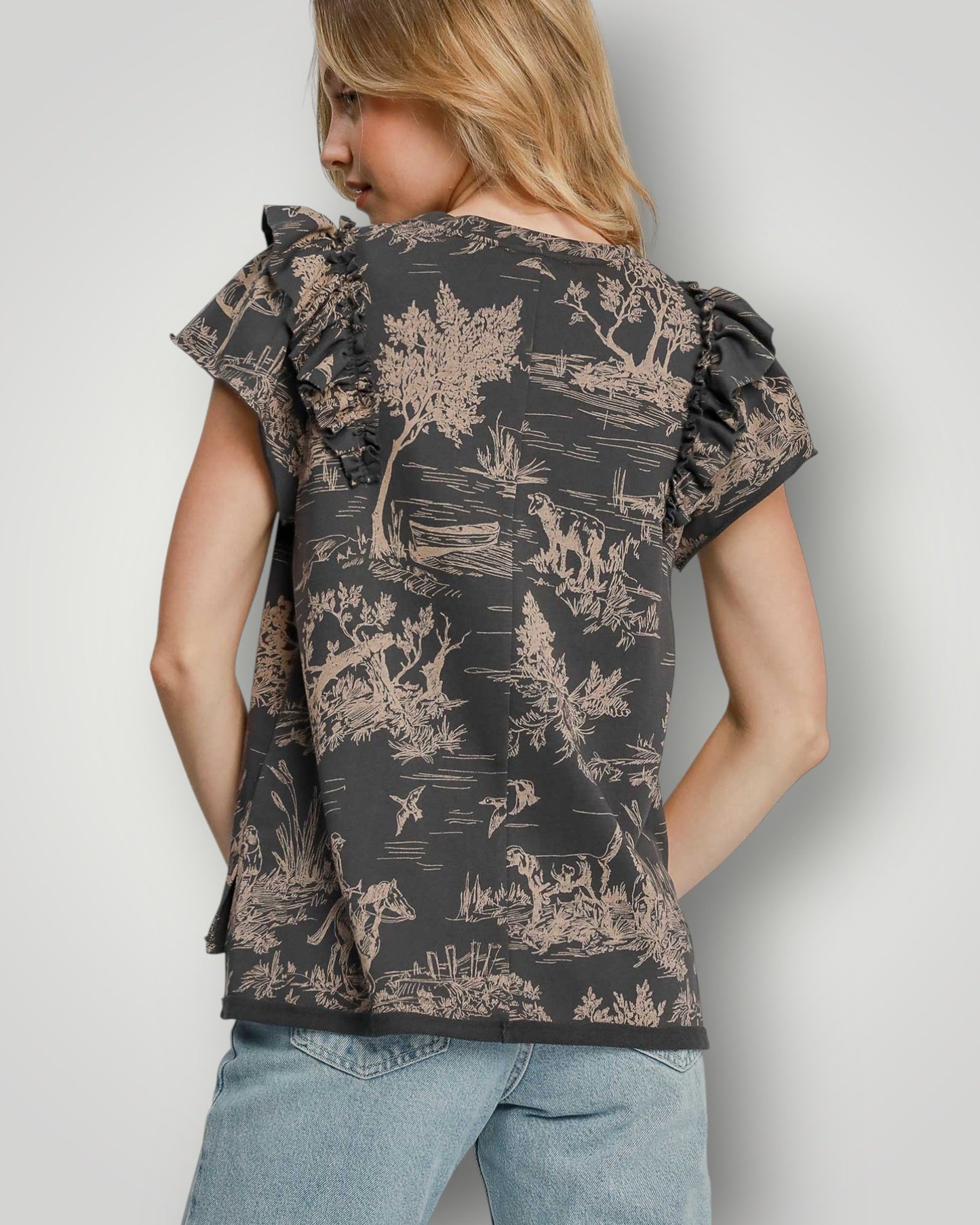 Woman wearing a floral patterned top with ruffled sleeves against a plain background