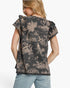 A woman shown from the back wearing a short-sleeve top with a beige toile-style print on a black background, paired with light blue jeans, against a plain white studio background.
