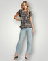 Woman wearing a patterned top and light blue jeans on a white background