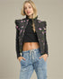 Woman wearing a black floral embroidered jacket and blue jeans on a beige background