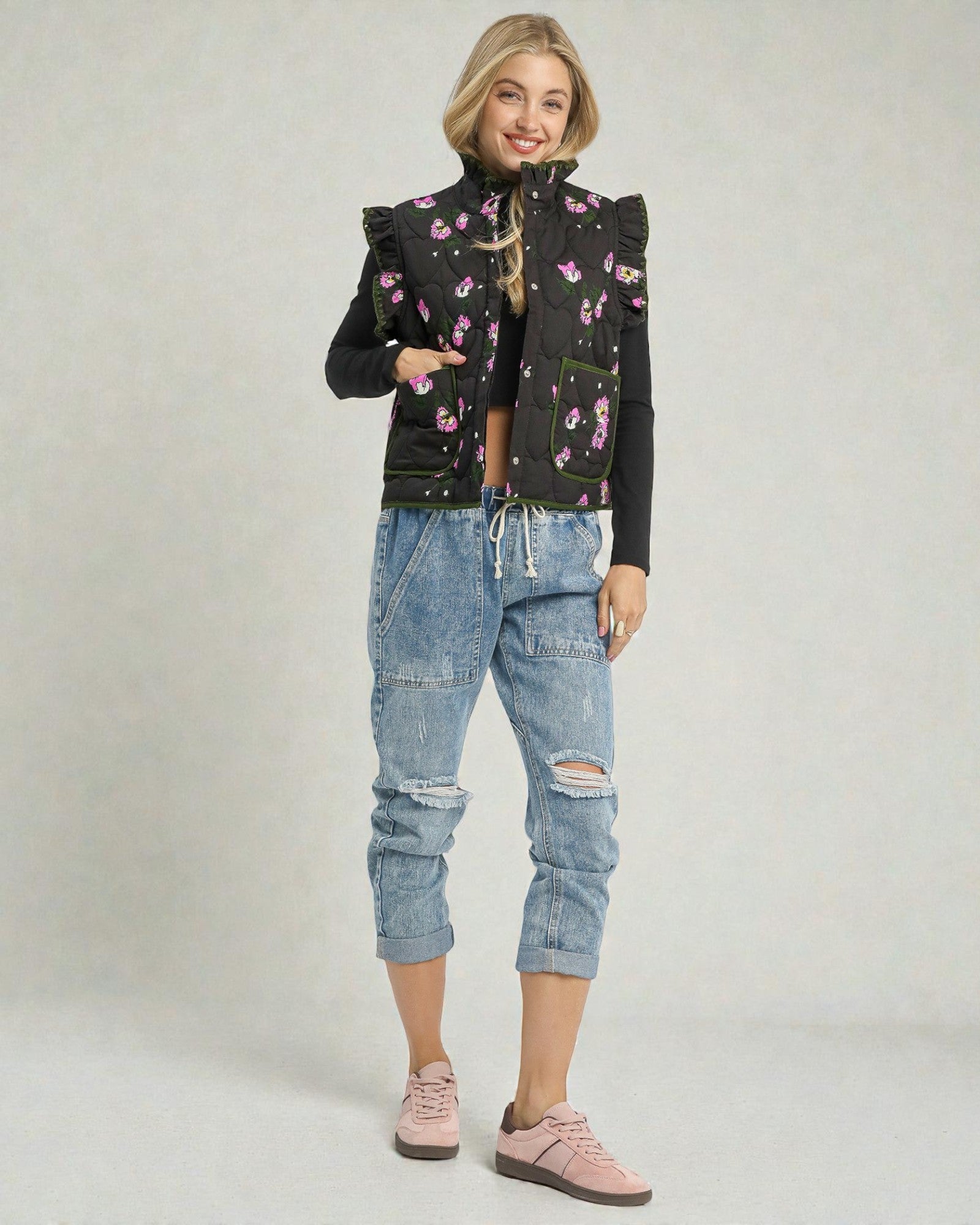 Woman wearing a floral patterned black jacket and blue jeans on a plain background