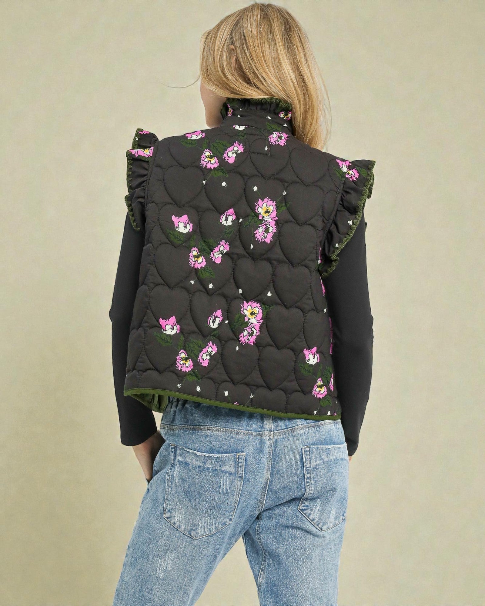 Person wearing a black quilted vest with pink floral patterns on a beige background