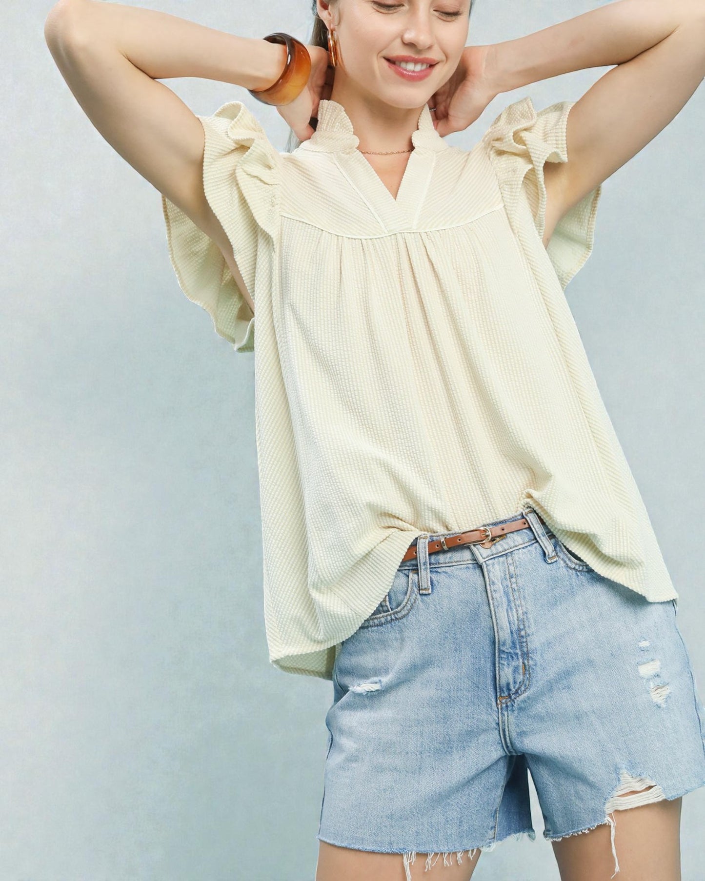 Woman wearing a light-colored blouse and denim shorts against a light blue background