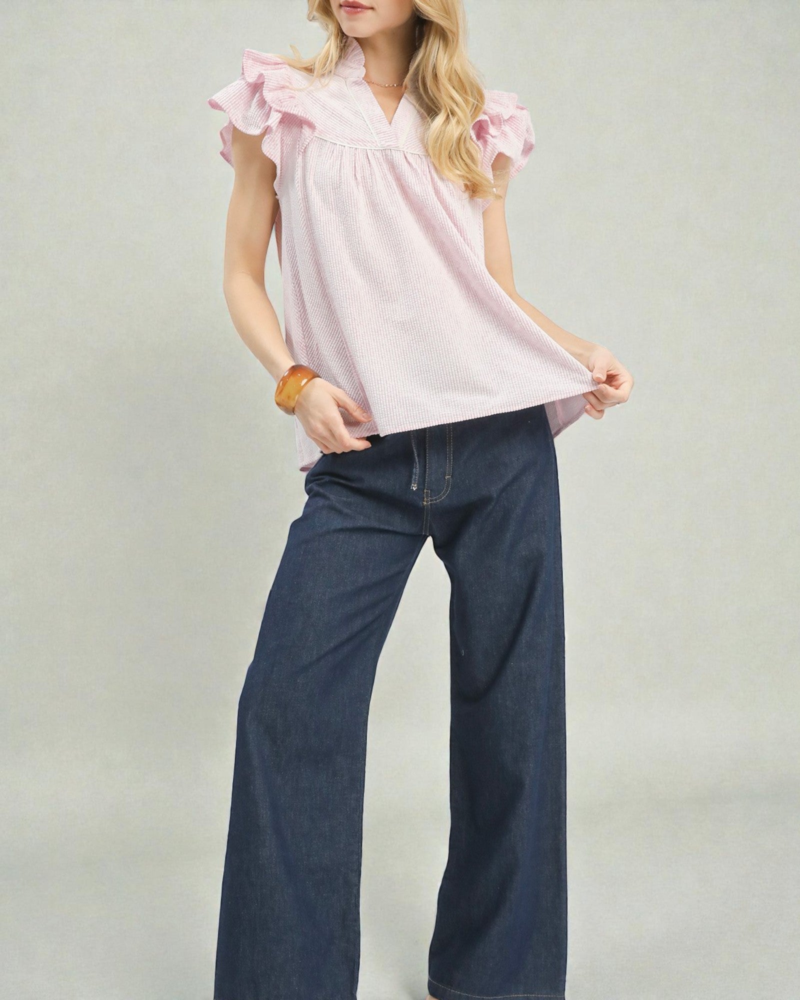Woman wearing a pink blouse with ruffled sleeves and dark blue jeans on a plain background