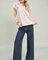 Woman wearing a pink blouse with ruffled sleeves and dark blue jeans on a plain background