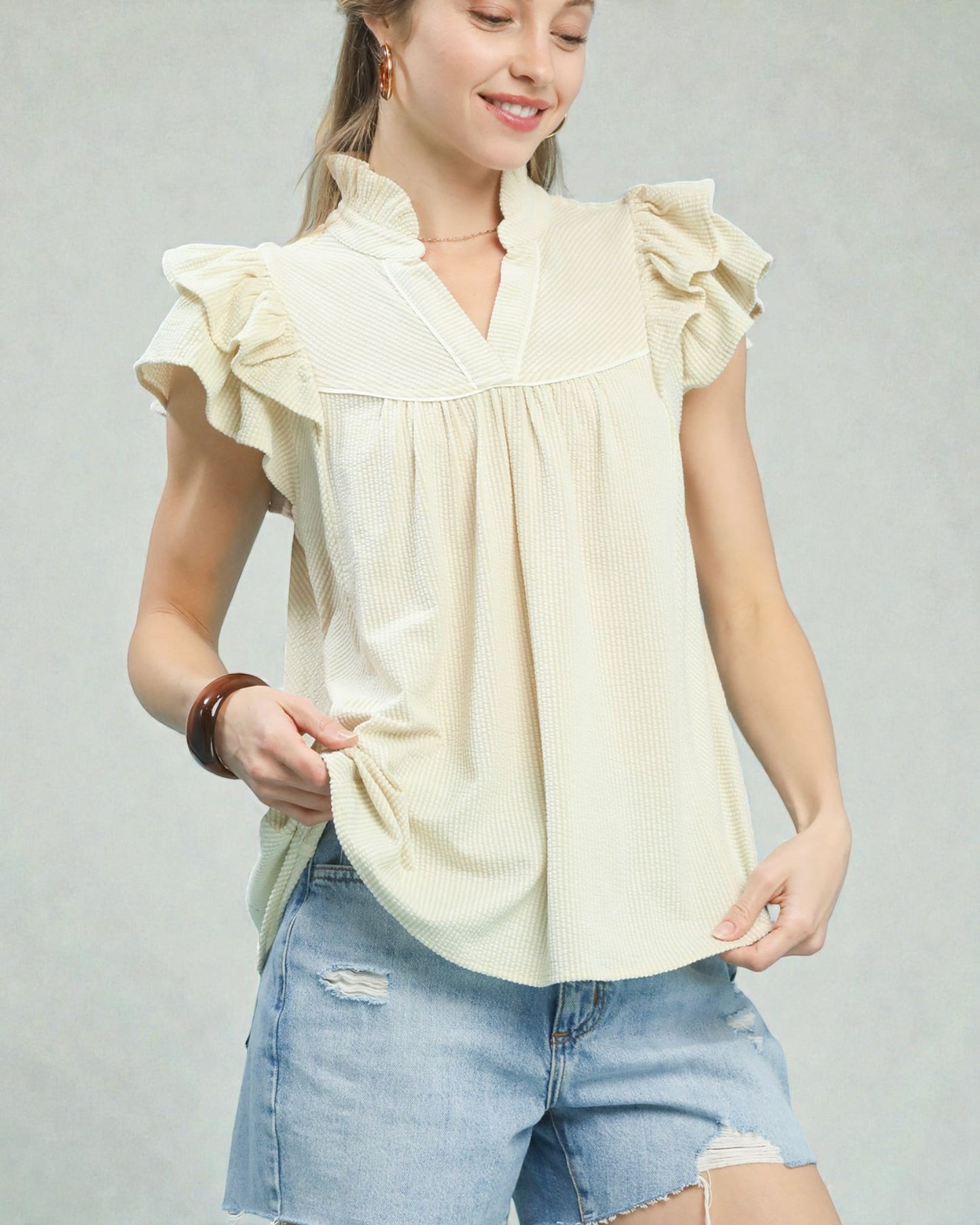 Woman wearing a light yellow blouse with ruffled sleeves and denim shorts on a gray background