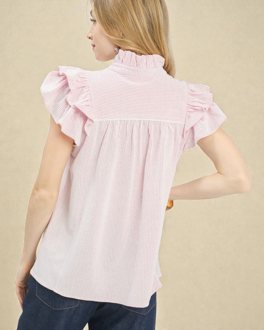 Woman wearing a pink striped blouse with ruffled shoulders on a beige background