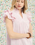 Woman wearing a pink dress with ruffled shoulders against a colorful floral background