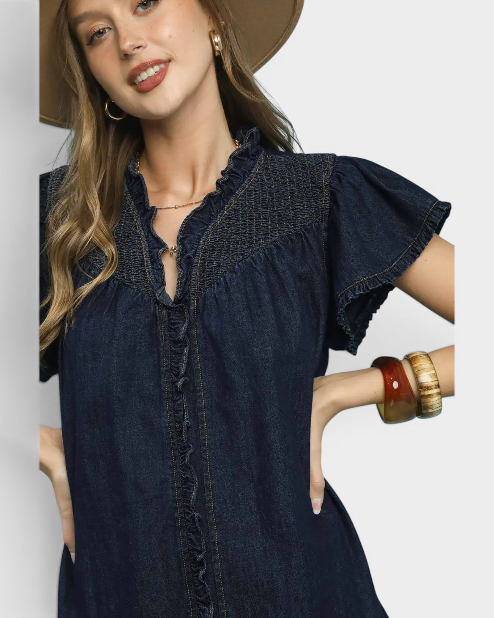 Woman wearing a dark denim dress with ruffled details on a plain background