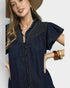 Woman wearing a dark denim dress with ruffled details on a plain background