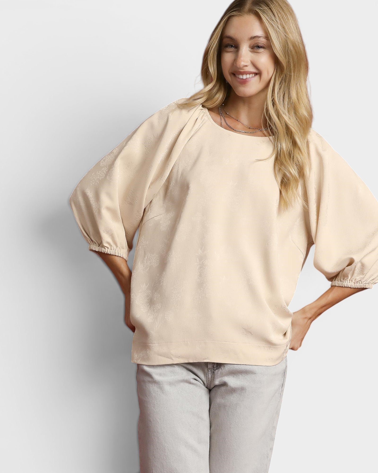 Woman wearing a beige blouse and light gray pants against a plain background