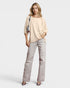 Woman wearing a beige top and light gray pants on a white background